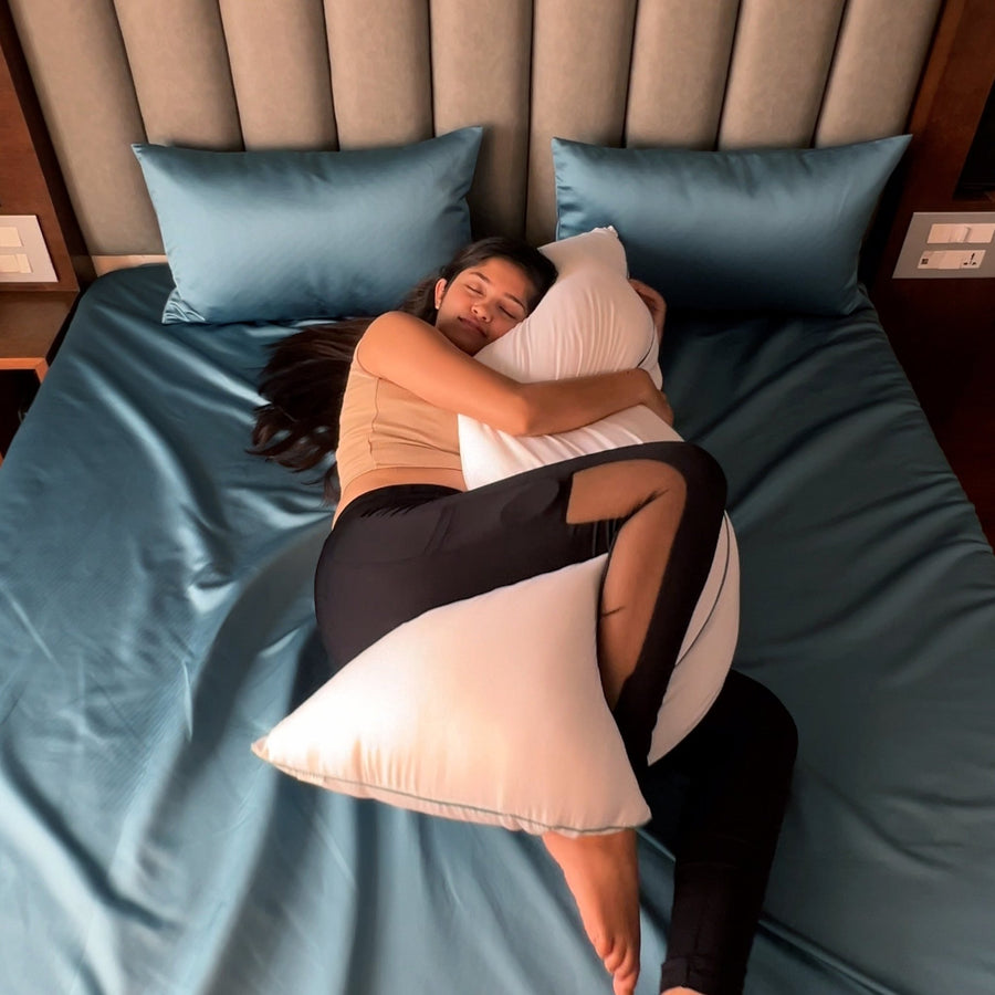 Side sleeper with the Seevo cuddle pillow between her arms and knees on teal satin bedding